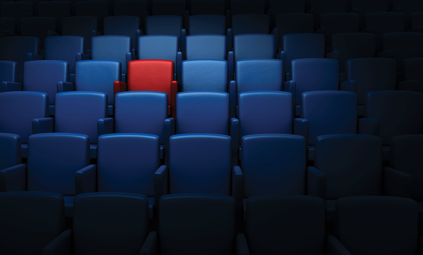A movie theatre full of blue seat with one red seat standing out on the top left corner