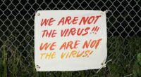 Sign on a fence that says we are not the virus, we are not the virus.