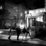 Students walking on a dark college campus towards a lit building