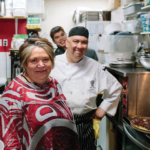 Three people including a chef standing in a cramped kitchen next to a stove