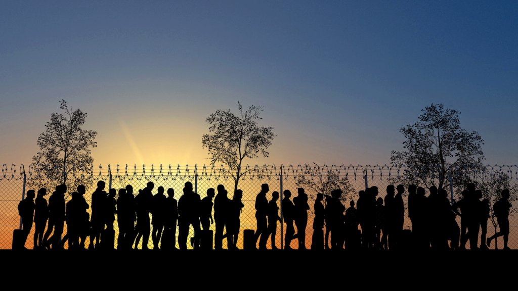 Sihlouettes of a group of people standing at a barbed wired fence at sunset