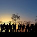 Sihlouettes of a group of people standing at a barbed wired fence at sunset