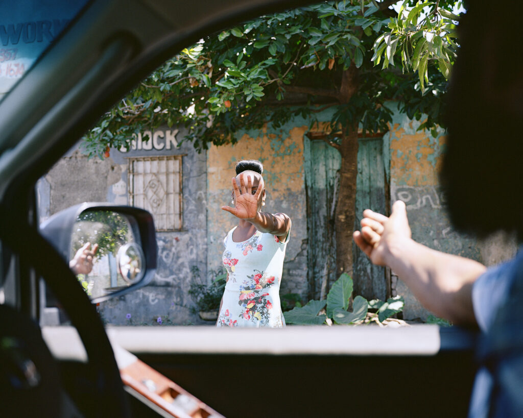 A photo by Andrew Jackson shows a woman reaching her hand out to a person in a car.