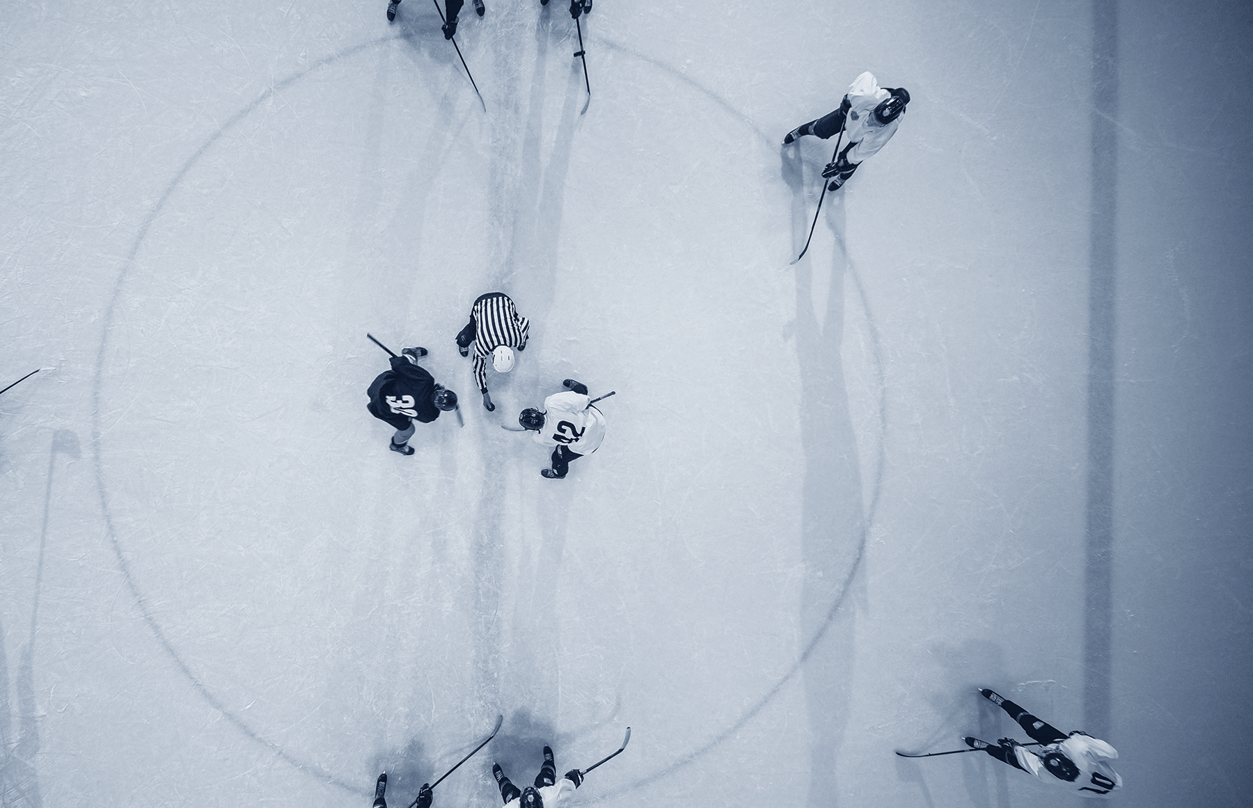 Black and white image, with a view from above of hockey players at centre ice awaiting the puck drop for a face off 