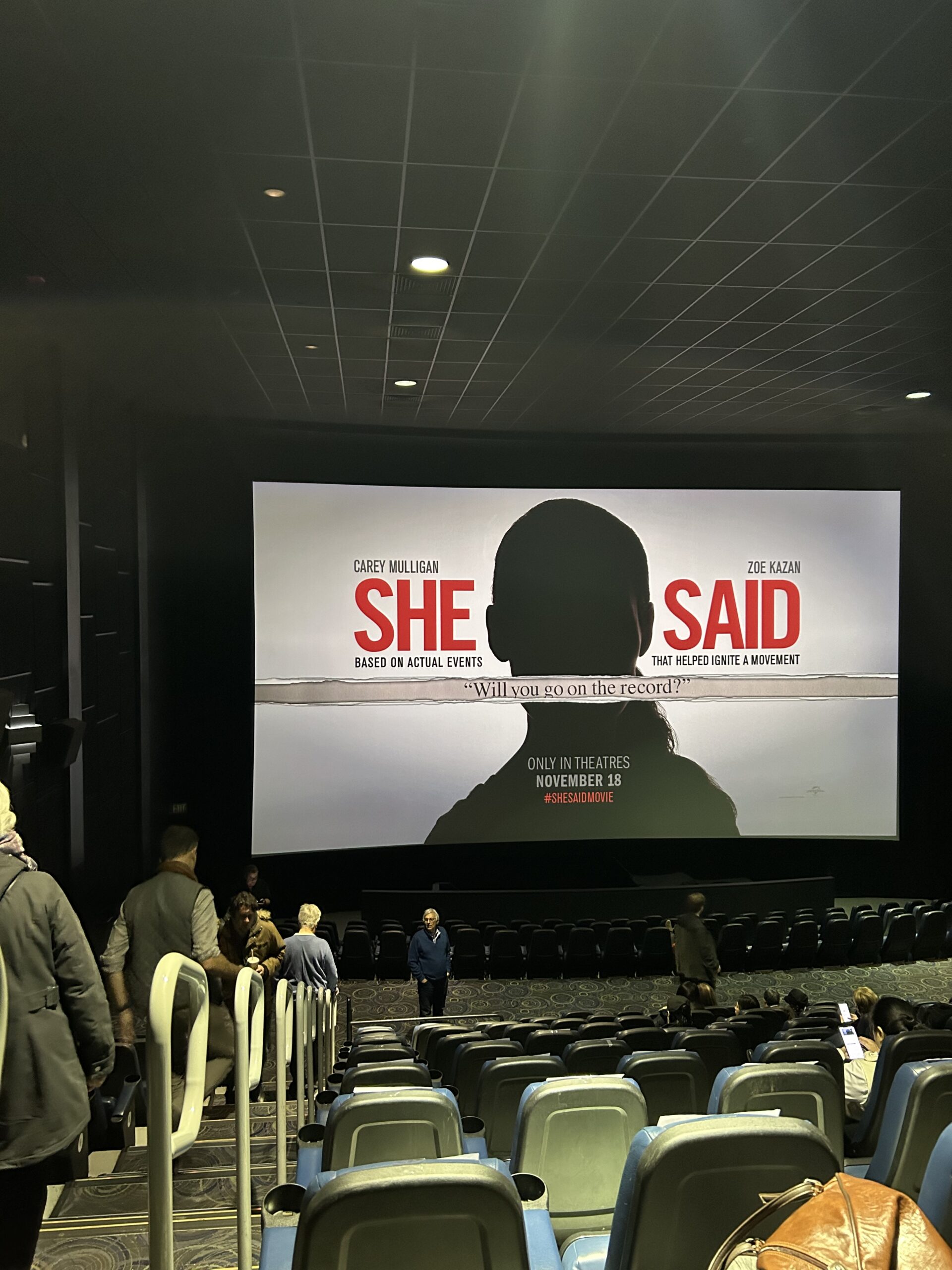 A photo of a movie theatre screen showing the poster for "She Said" at an advanced screening of the movie. 