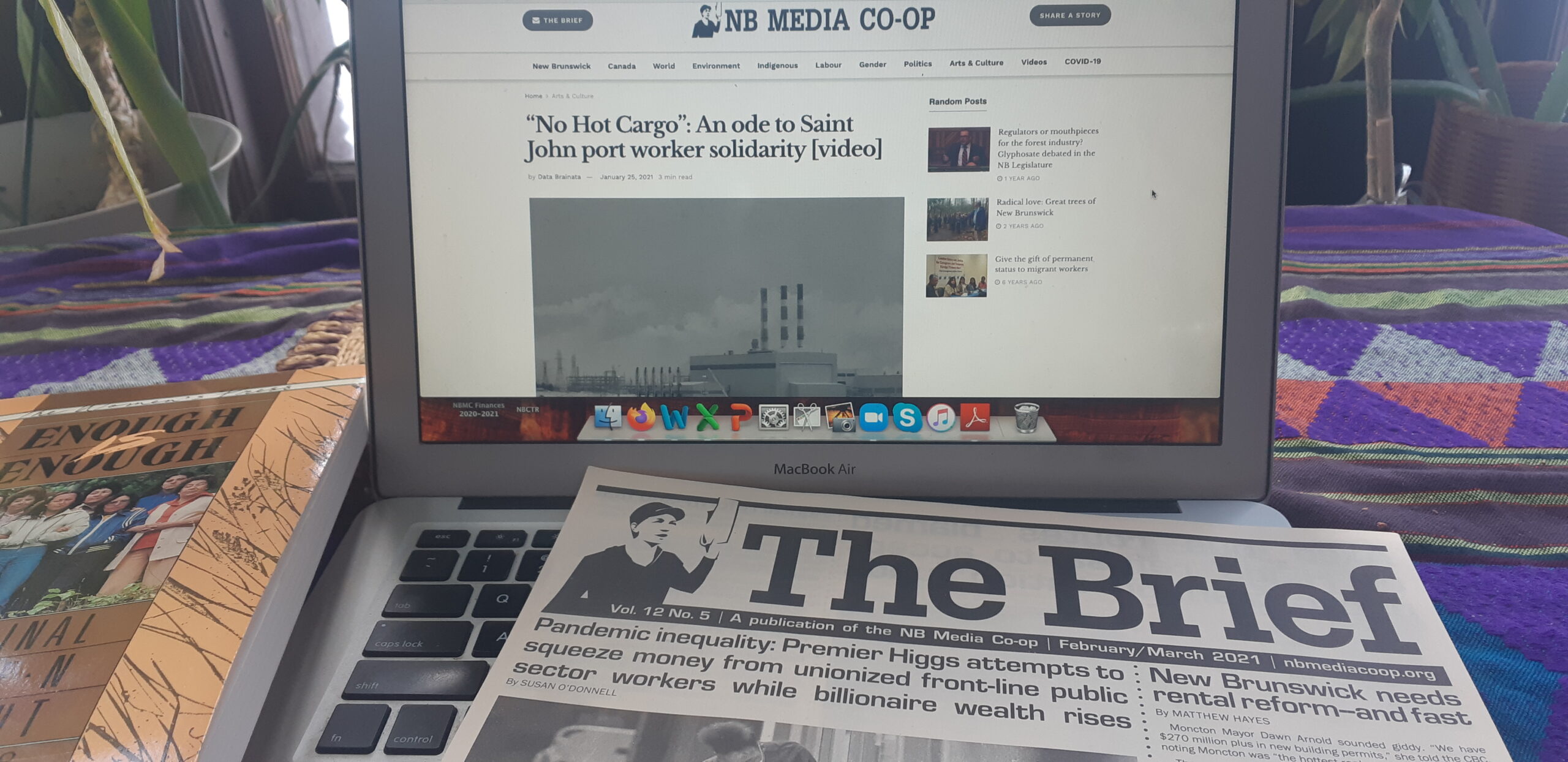A copy of NB Media Co-op's newsletter "the Brief" sits on the keyboard of a laptop showing the Co-op's website. 