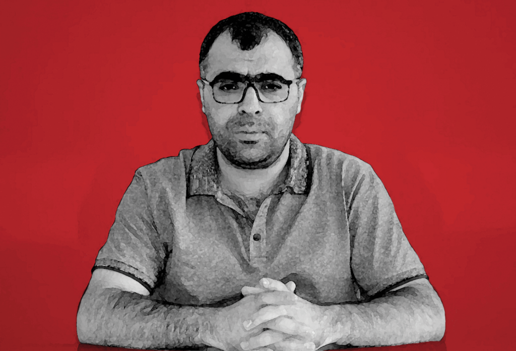 Sinan Aygül in black and white, looks into the camera, against a red backdrop