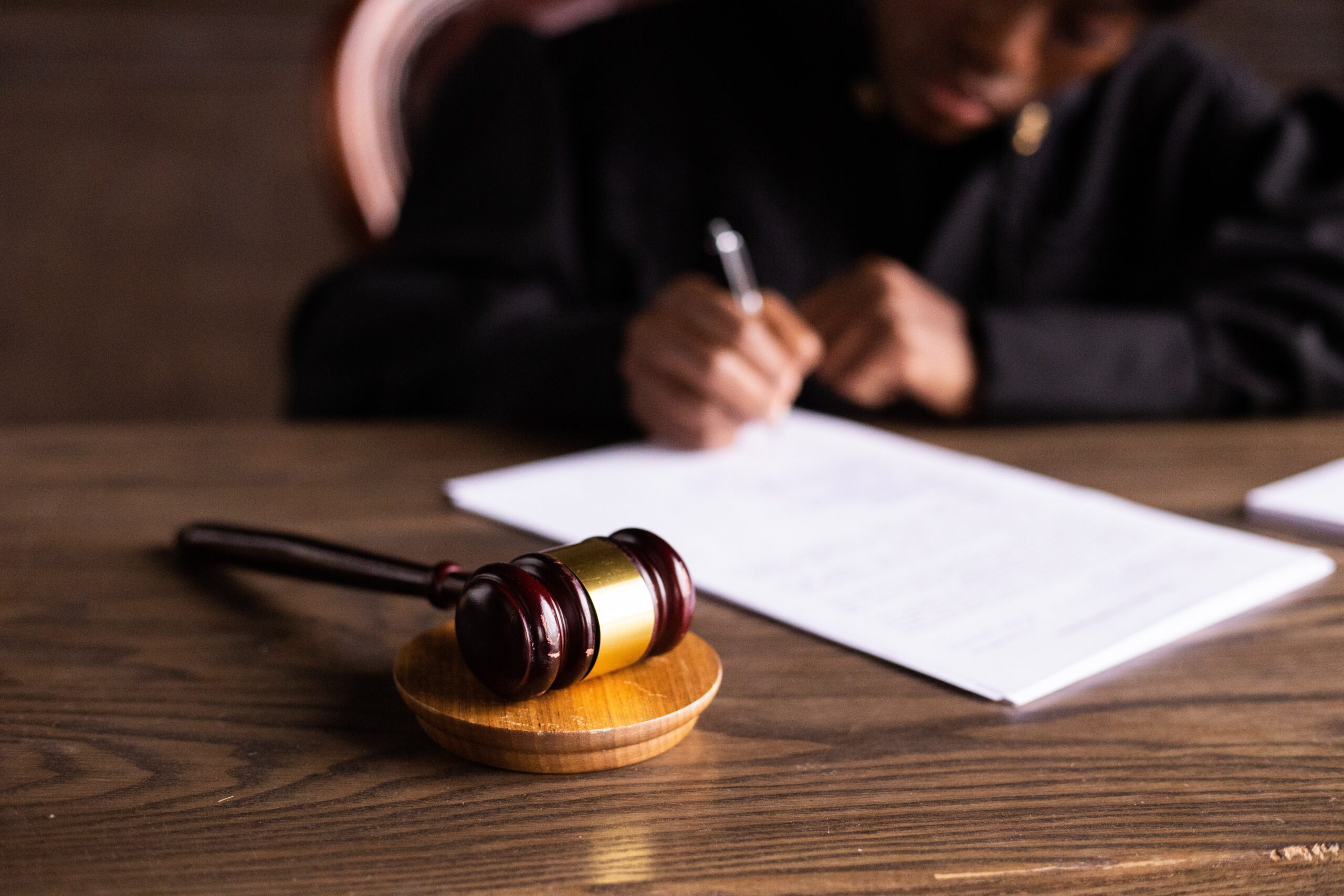 A lawyer sits at their desk, writing something on a piece of paper in the background and out of focus. In front of them is a gavel.