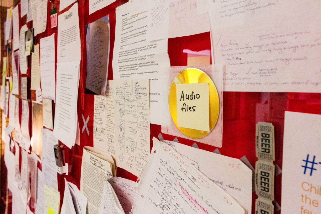 Archived handrwritten notes and a CD are showcased on a red wall.