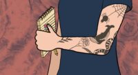 A tattooed arm holds a pen and a notepad