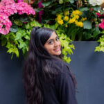 A portrait of a woman looking back at the camera, standing in front of flowers.