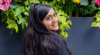 A portrait of a woman looking back at the camera, standing in front of flowers.