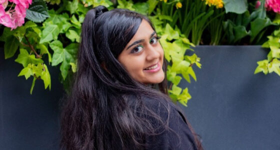 A portrait of a woman looking back at the camera, standing in front of flowers.