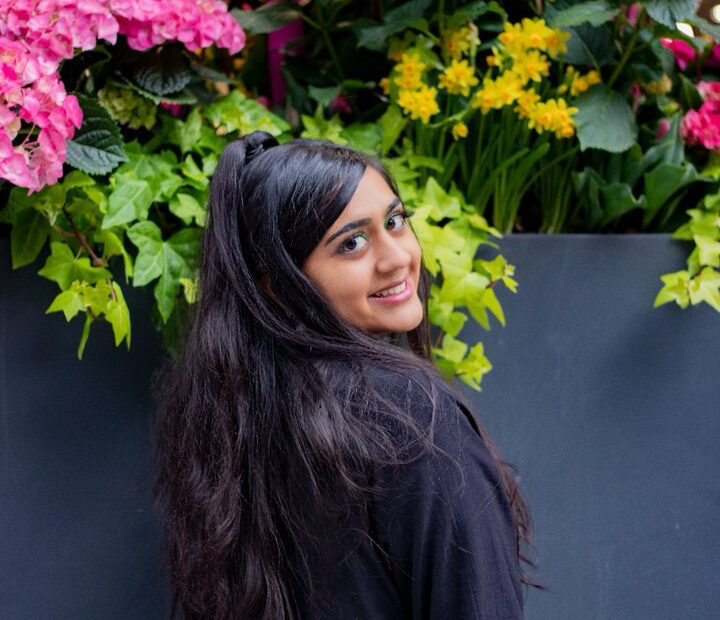 A portrait of a woman looking back at the camera, standing in front of flowers.