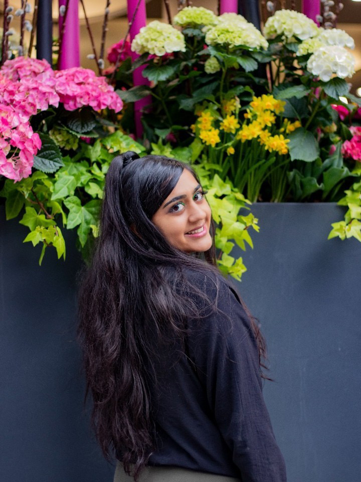 A portrait of a woman looking back at the camera, standing in front of flowers.