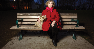 Stevie Cameron sits on a park bench with her dog at night
