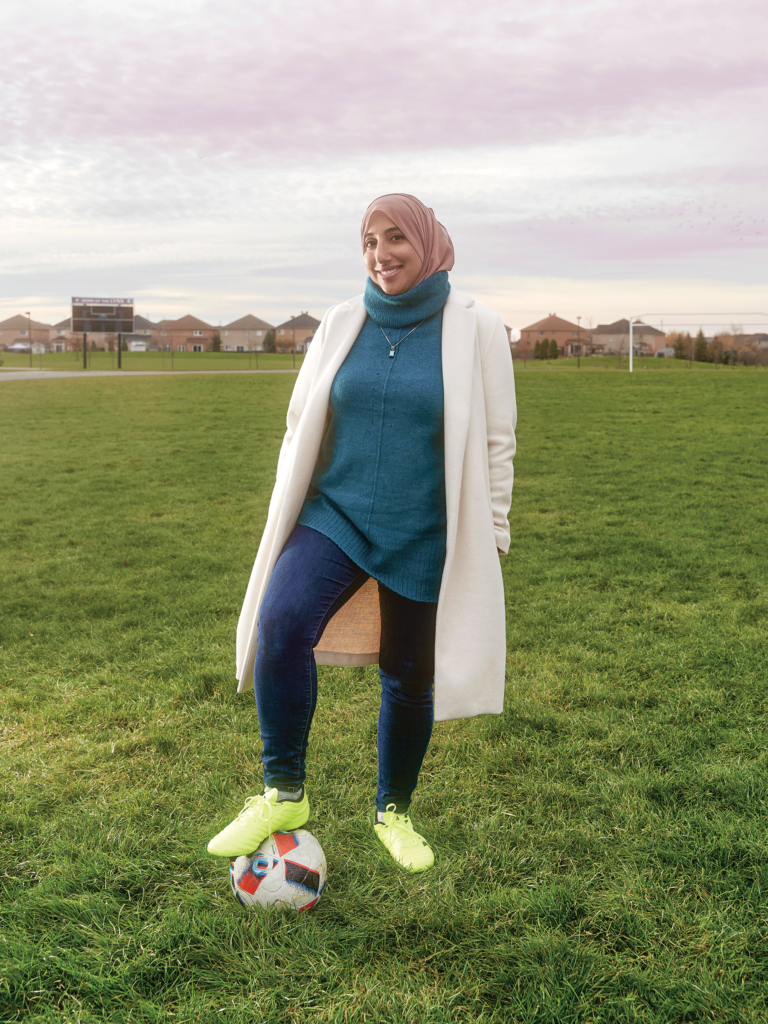 Shireen Ahmed wears yellow soccer shoes and stands with a ball under her foot on a soccer pitch