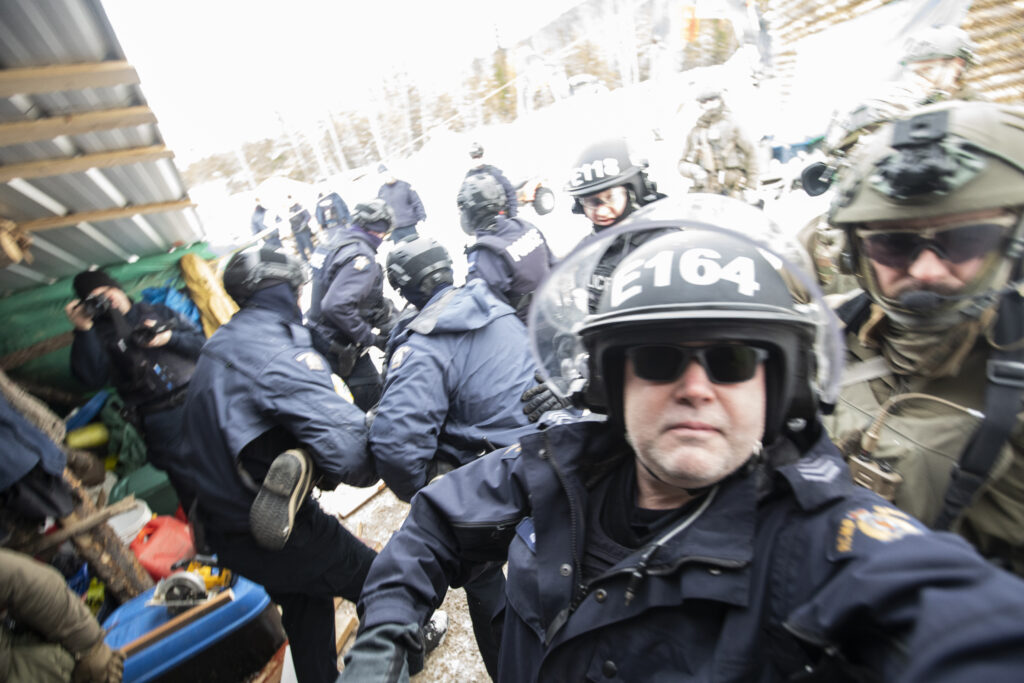 A person being carried away by a group of police officers wearing helmets with one officer facing forward