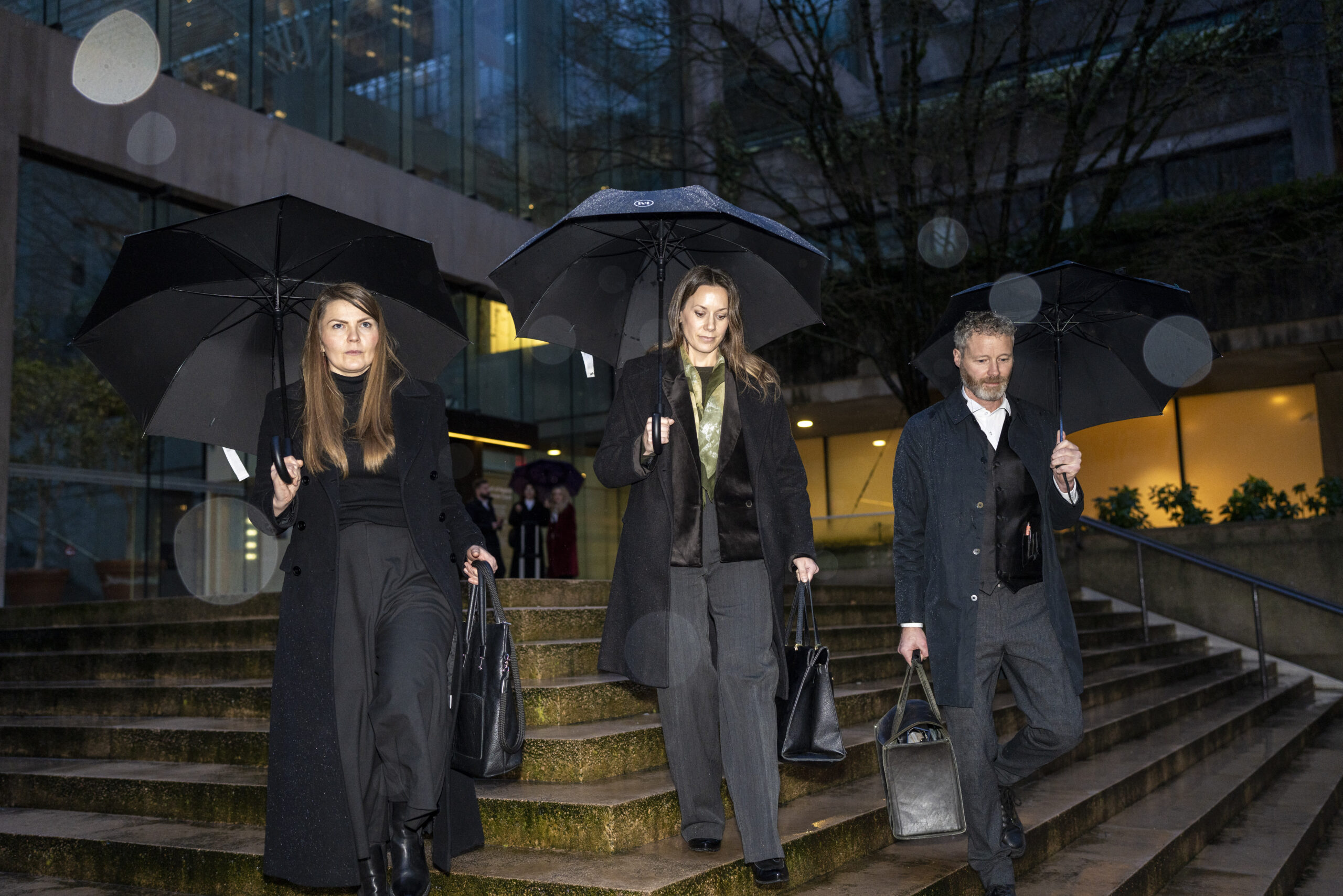 A photo of three people walking down stairs holding umbrellas and large handbags.