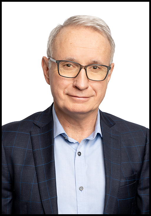 A photo of a man with white hair wearing glasses, a navy blue blazer and a baby blue dress shirt in front of a white background.