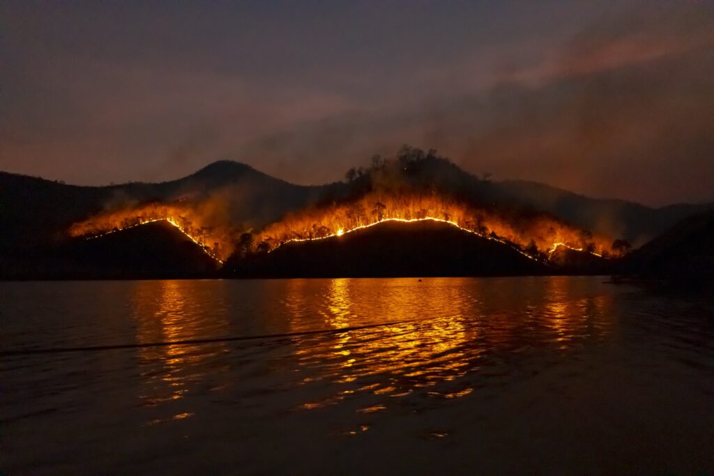 A landscape photo of a forest on fire that's surrounded by water.